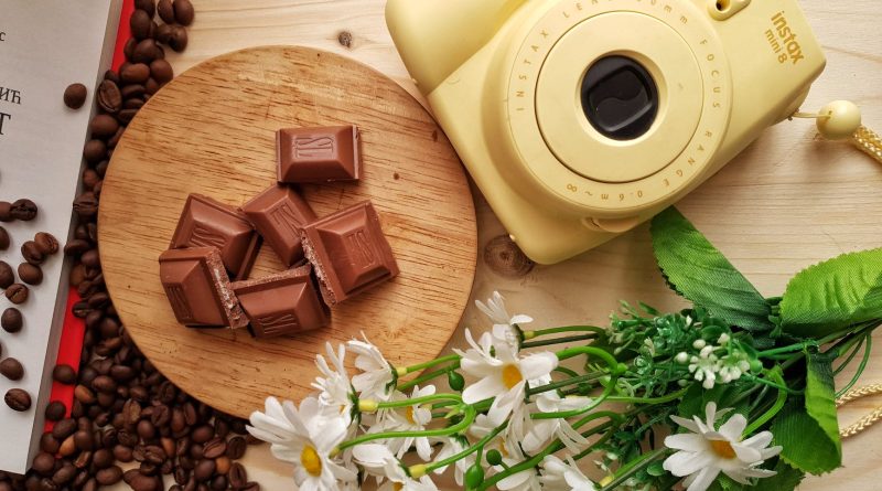 instant photo camera near chocolate and spilled coffee beans indoors